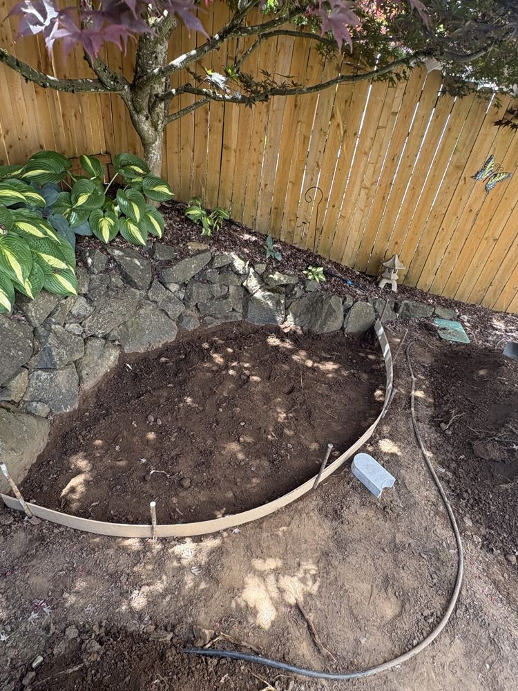 Forms set for a curved backyard patio along a rock wall