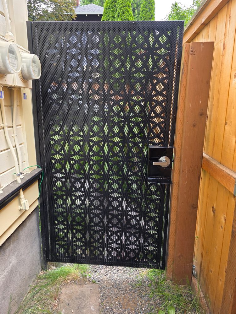 Custom black steel walk gate with a laser-cut geometric privacy panel and lever lockset