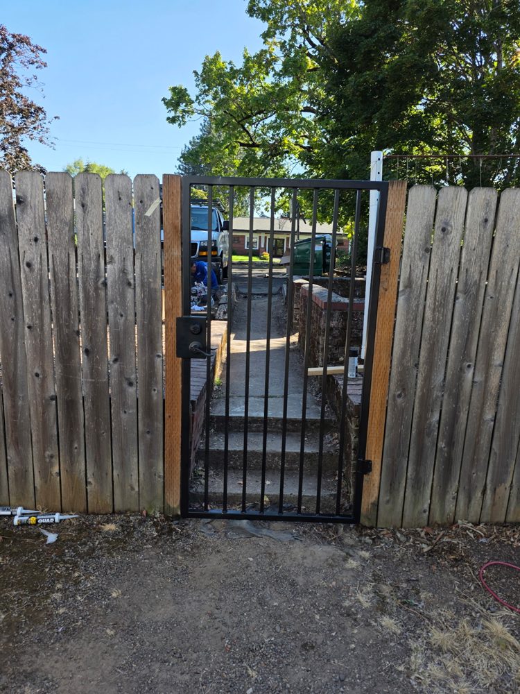 Steel picket walk gate installed in a wood fence with a keyed deadbolt and lever