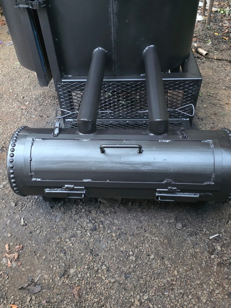 Close-up of the smoker firebox with riveted end caps, latching door and twin heat tubes