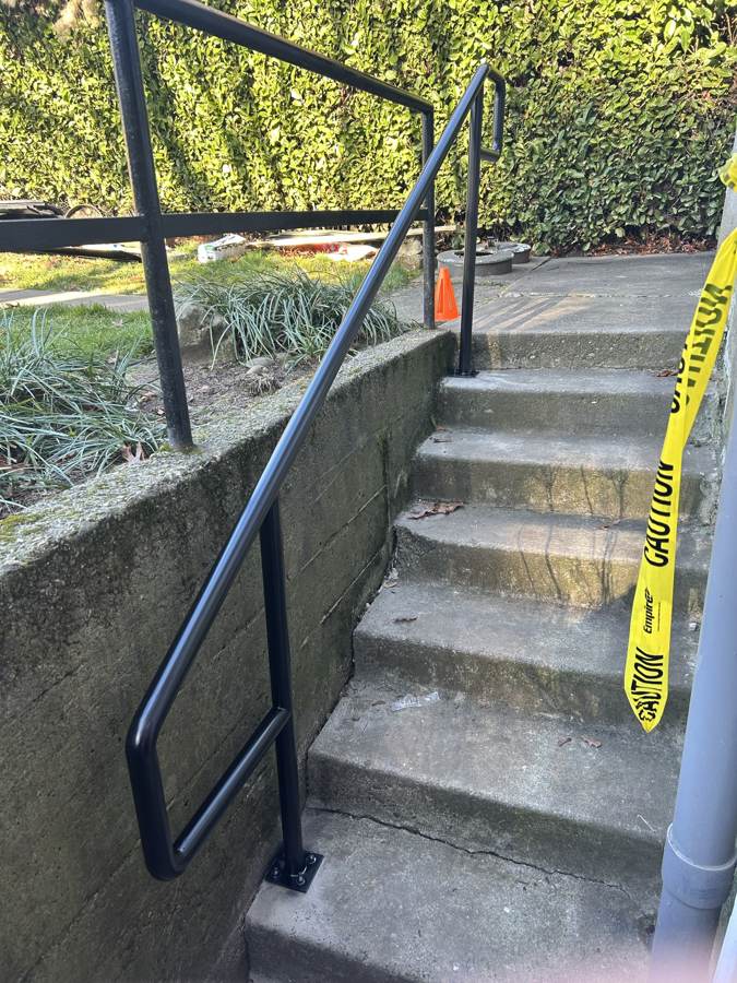 Black steel handrail running down concrete stairs