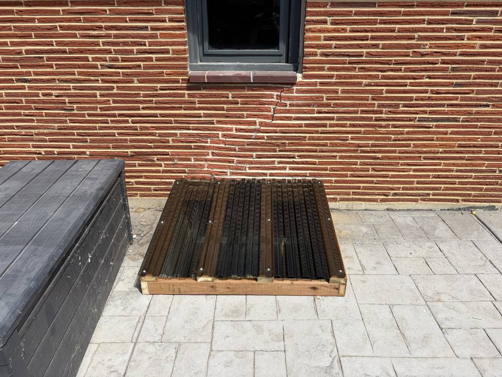 Window well cover installed beside a brick wall