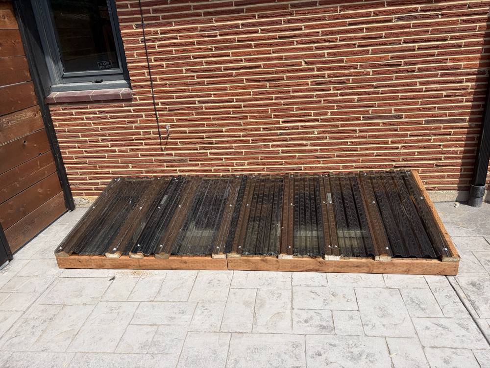 Window well cover along a brick wall and patio