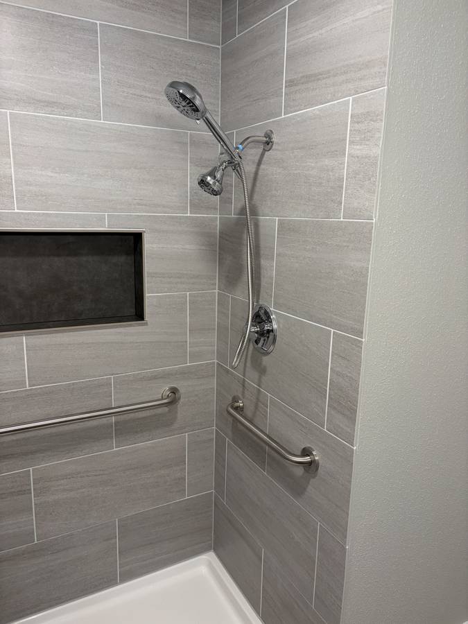After: large-format tile with a handheld shower and grab bars
