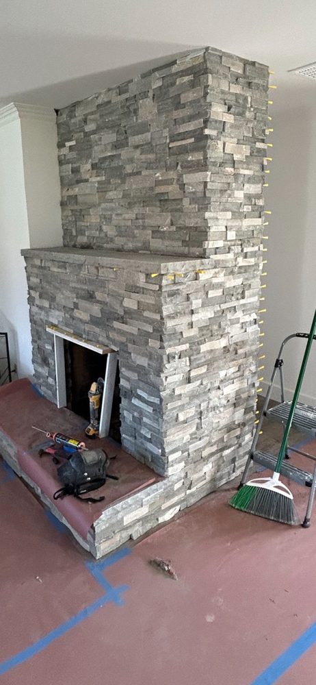 Floor-to-ceiling stacked stone fireplace with hearth and mantel during install