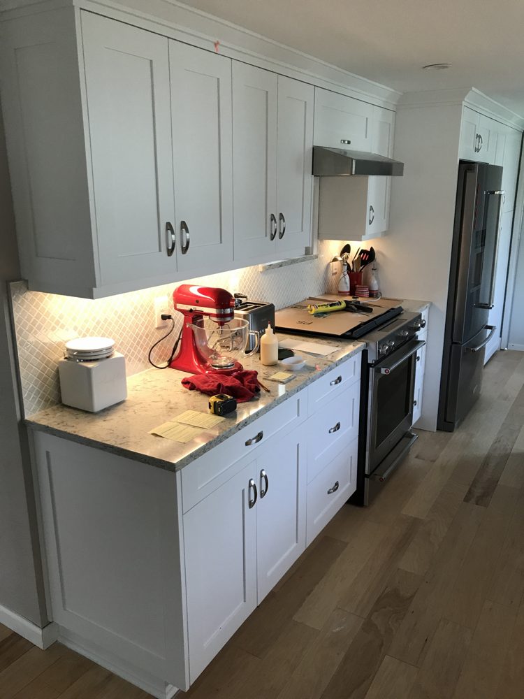 Kitchen with white shaker cabinets, quartz countertop, tile backsplash and under-cabinet lights