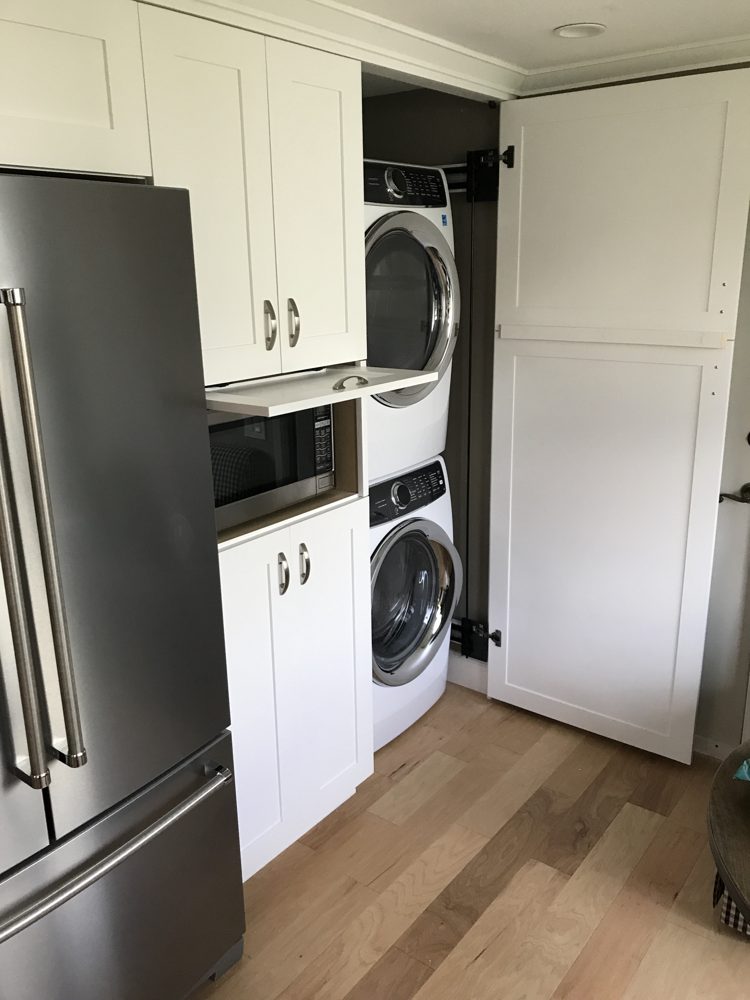 Stacked washer and dryer hidden behind a full-height cabinet door, with a microwave nook